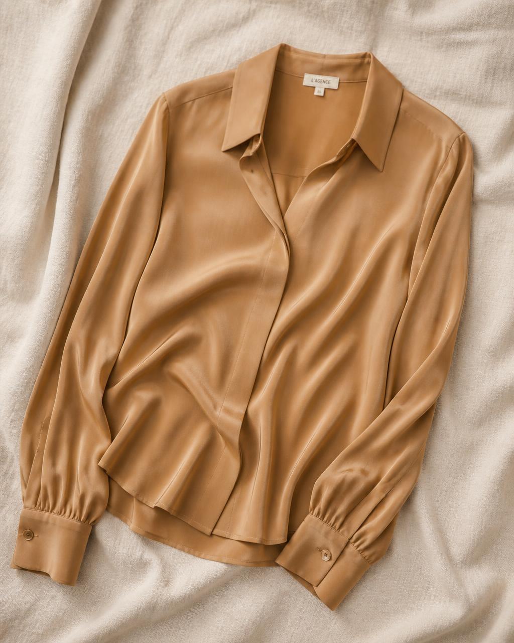A caramel silk blouse laid on cream linen